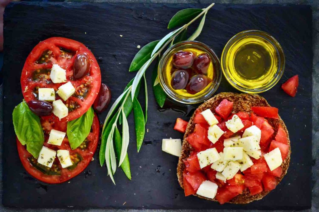 slices and diced tomatoes with cheese, basil, and small bowls of olive oil and olives on black background
