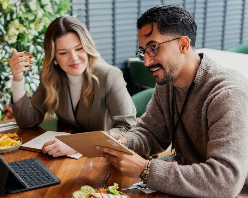 Two professionals discussing ideas over lunch while looking at a tablet